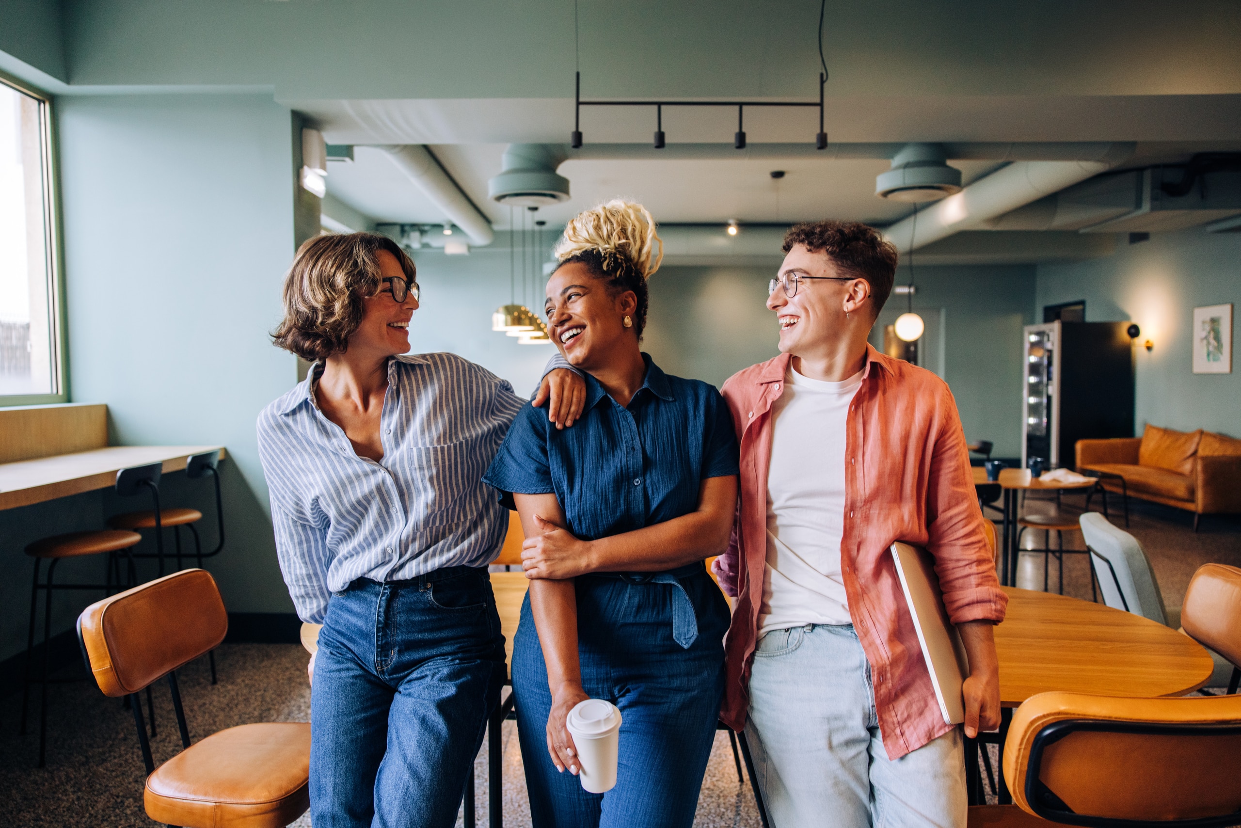 Group of young professionals smiling and enjoying each other's company in an office Three young professionals standing together in a casual office setting. They exhibit a friendly and cheerful demeanor, emphasizing positive connections and professional relationships.