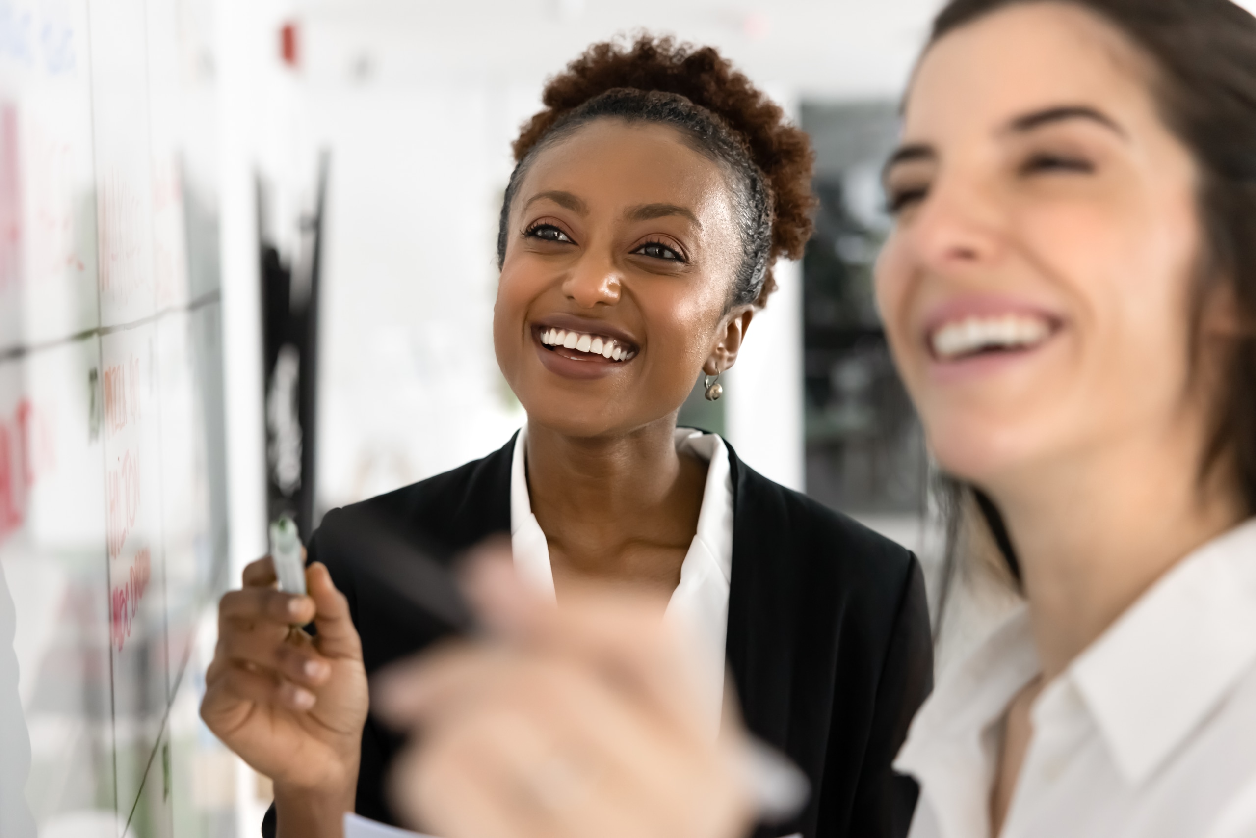 Two happy women marking successful milestone or completed tasks on calendar, discuss future plans, feel optimistic while creating visual representation of goals and timelines on white board, close up