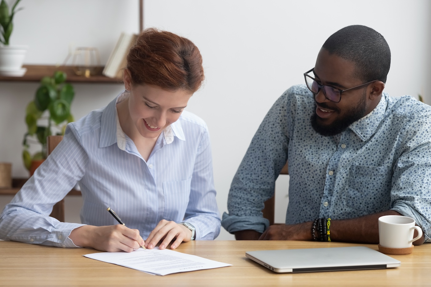 Image 3 Young attractive woman candidate sitting at desk with black company executive manager getting hired signing job contract feels happy. Satisfied client affirming selling or buying agreement at agency