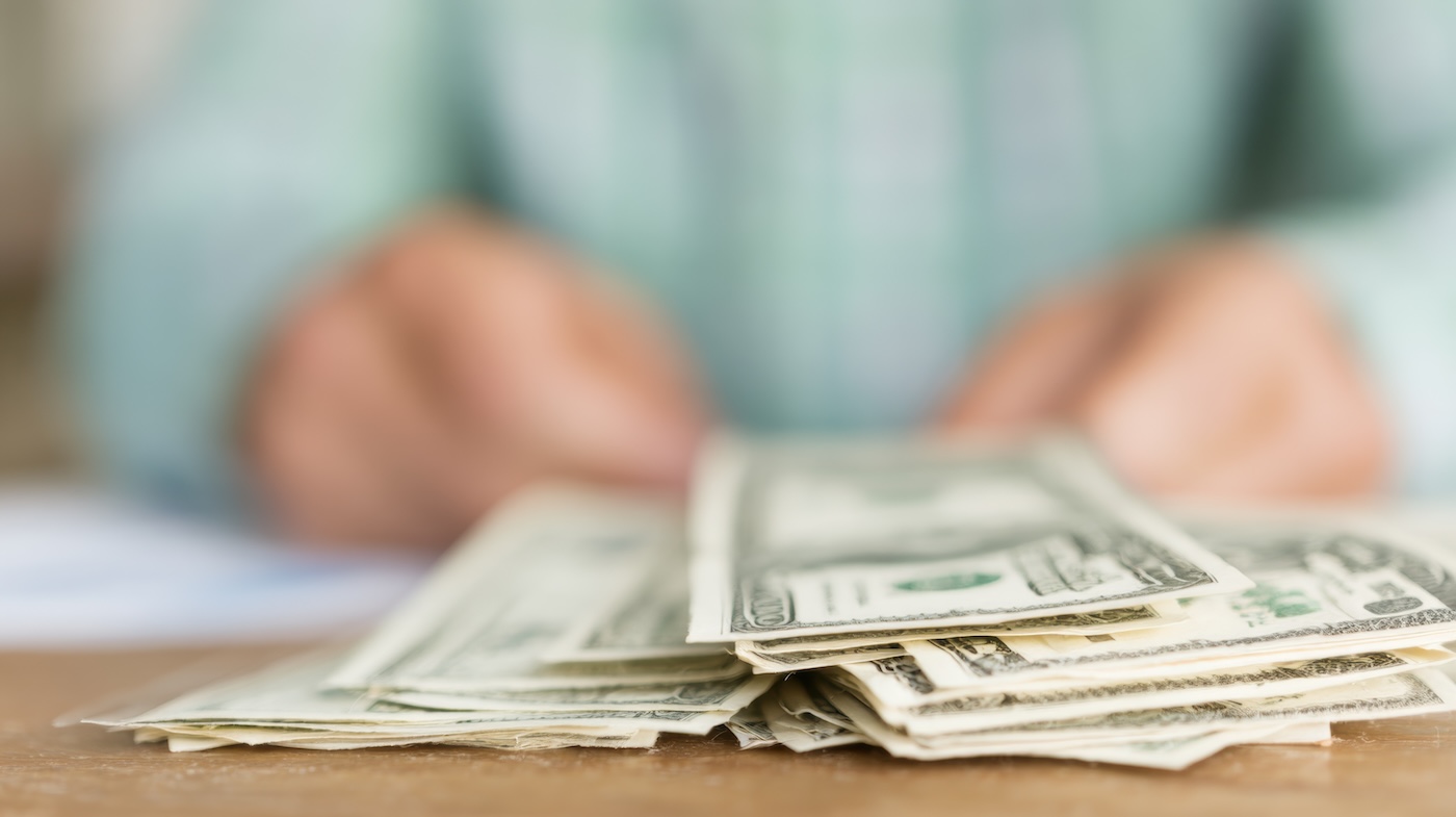Capa A person is counting cash on a wooden desk while preparing for a transaction in an office setting.