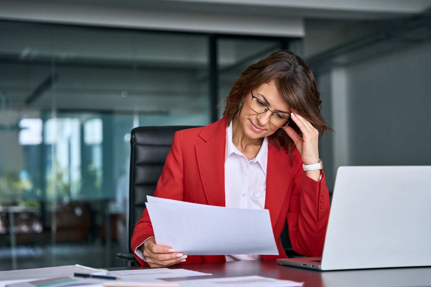 Image 1 Confused mature trader businesswoman looking disappointed at loan tax paper document using laptop pc computer having stress. Business woman ceo holding hand near temples, feeling stressed in office