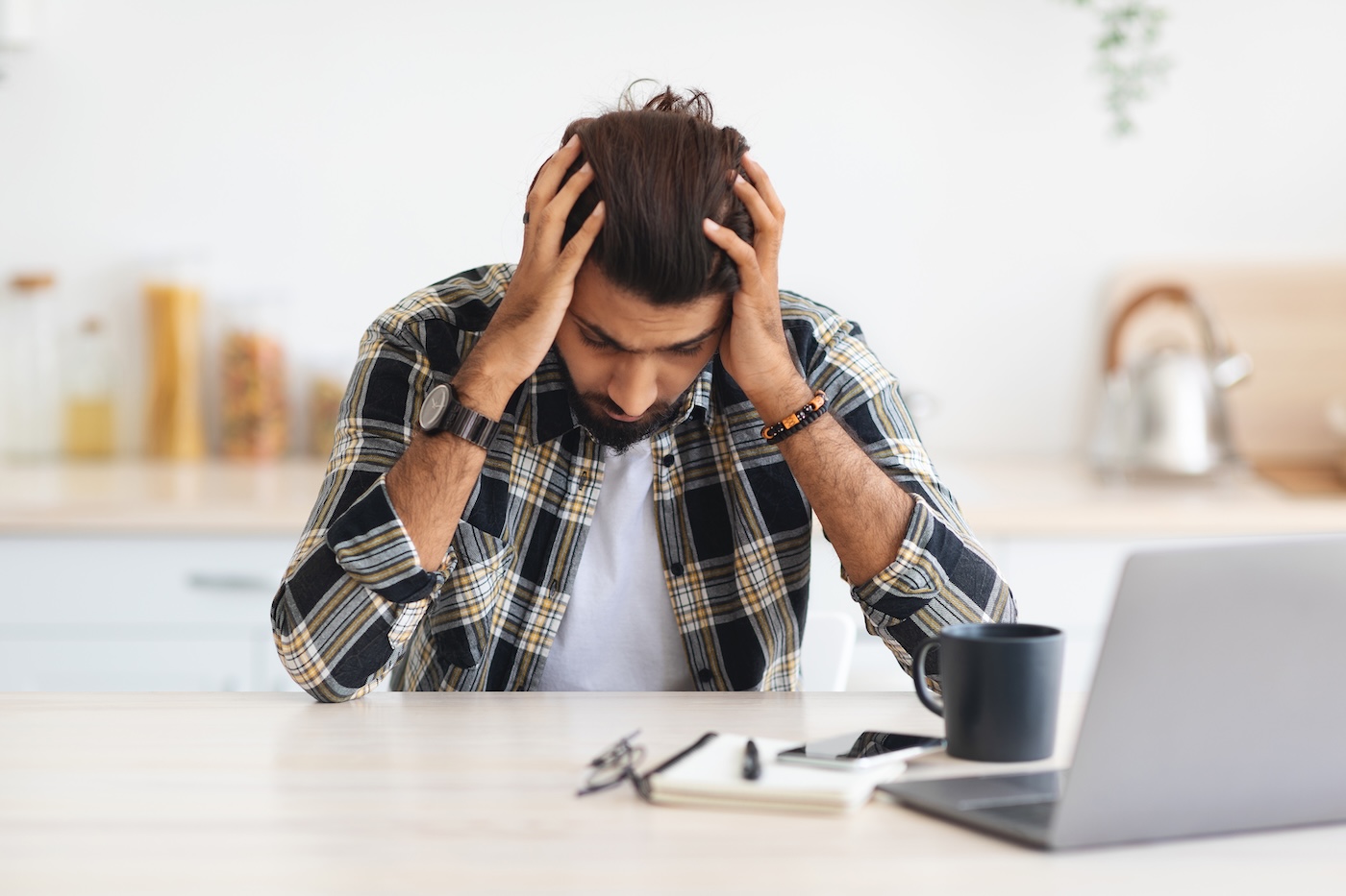 Image 4 Depressed arab man sitting in front of laptop at home, touching his head, suffering from burnout or financial crisis, young middle-eastern freelancer having problems at job, copy space